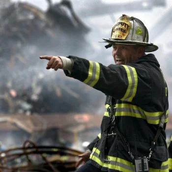 A volunteer firefighter in a black and yellow uniform holding a fire hose