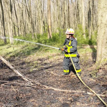 A volunteer firefighter in a black and yellow uniform holding a fire hose